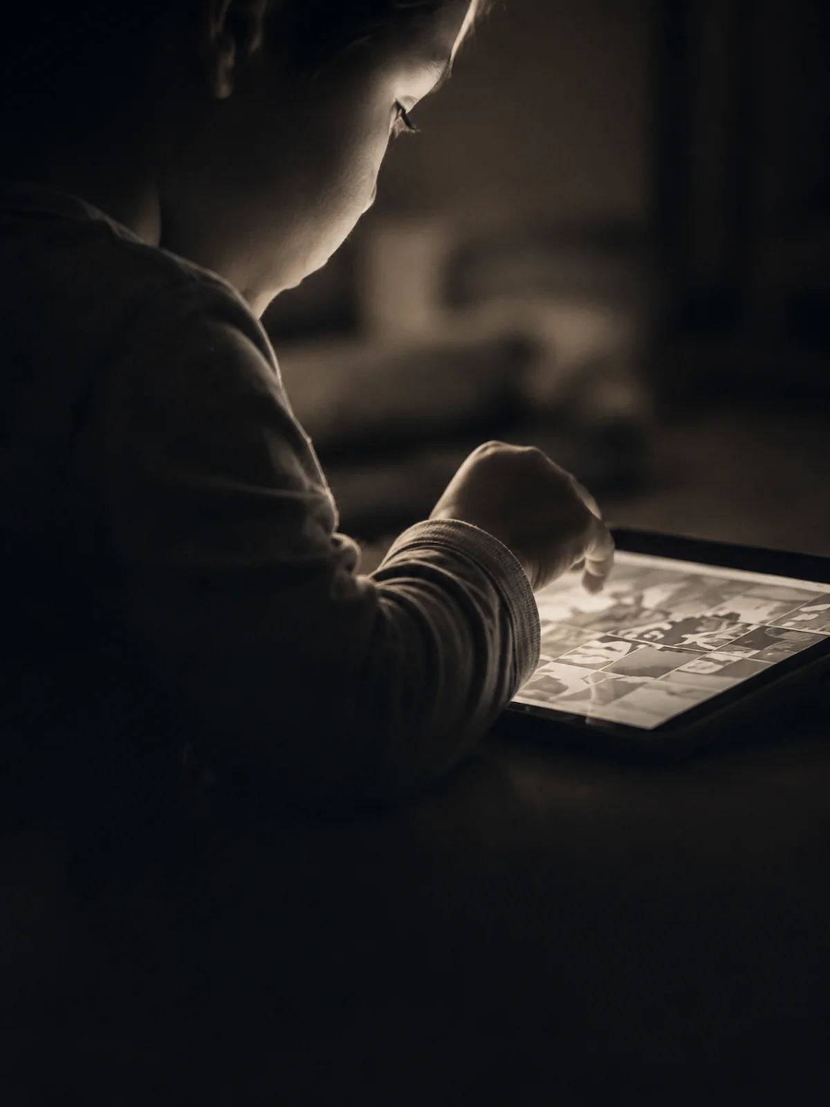Criança em ambiente escuro com tablet iluminando o rosto